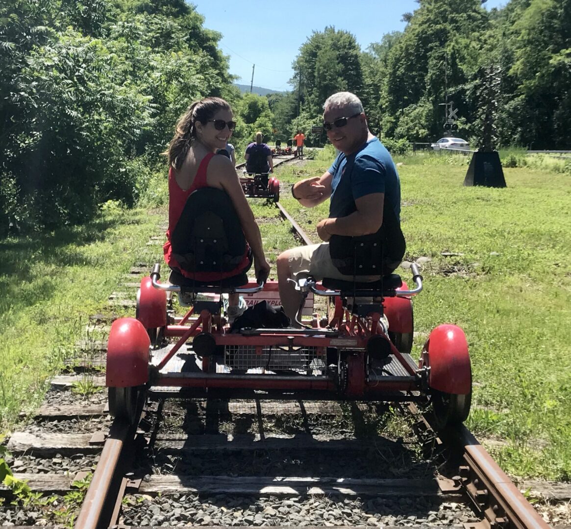 A man and woman riding on the back of a red train.